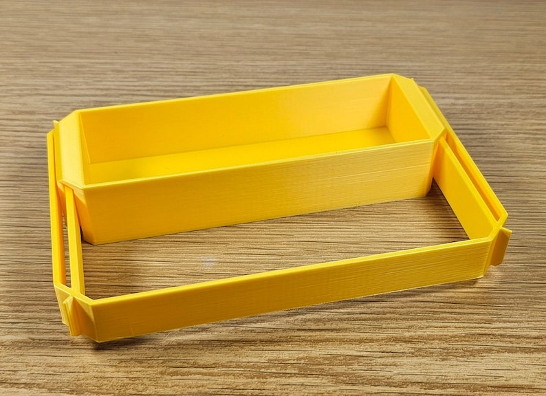 Op de afbeelding: Een gele plastic opbergdoos met deksel. De doos is gemaakt van 3D-geprint plastic en heeft een glad, getextureerd oppervlak.