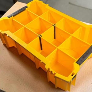 May include: A bright yellow plastic storage organizer tray featuring multiple compartments separated by removable black dividers. The rectangular unit has the text TOUGHSYSTEM embossed on two black side handles, providing a structured layout for organizing small tools, hardware, or various components.