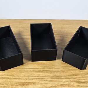 May include: Three black rectangular boxes made of plastic. The boxes are empty and have a smooth surface.