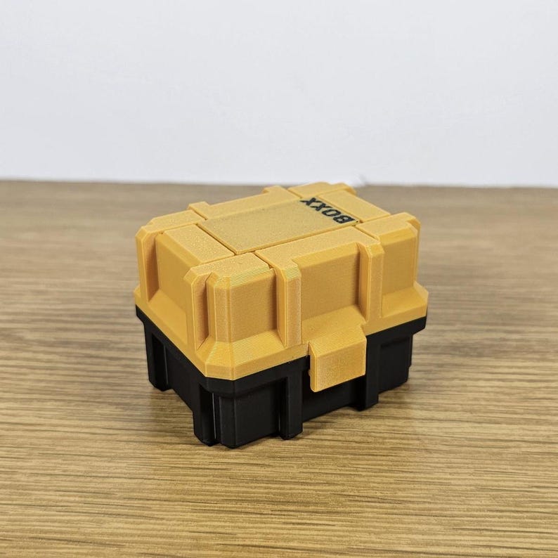 May include: A small, yellow and black box with the word "BOXX" printed on the top. The box is made of plastic and has a textured surface.