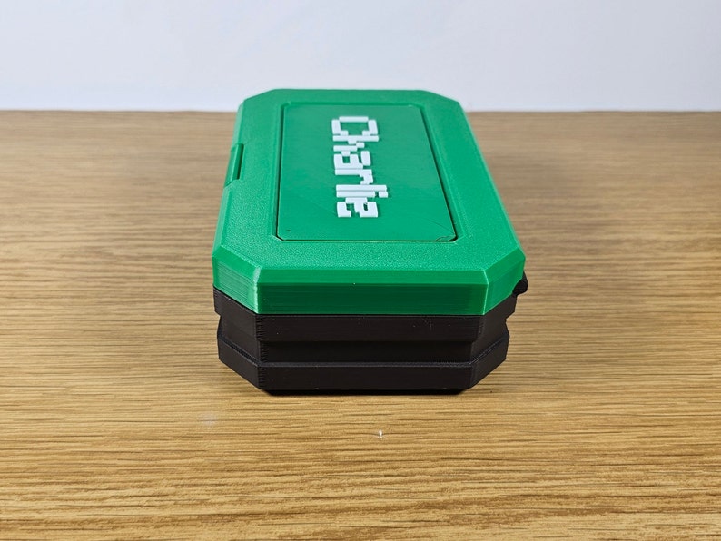 May include: A green and black plastic storage box with the word "Charlie" printed on the top.