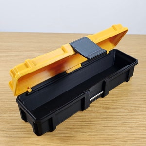 May include: A small black and yellow plastic storage box with a hinged lid. The lid is open and the box is empty.