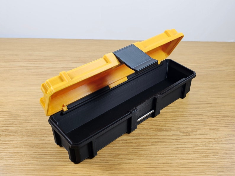 May include: A small black and yellow plastic storage box with a hinged lid. The lid is open and the box is empty.