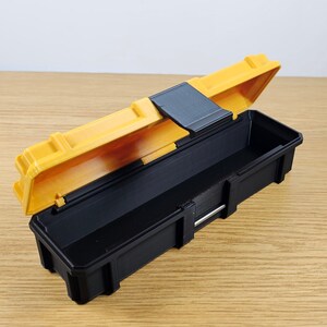 May include: A small yellow and black plastic tool box with a latch. The lid is open and the inside of the box is black.
