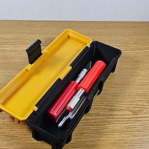 May include: A black and yellow plastic case with a latch, open to reveal four utility knives with red and silver handles.