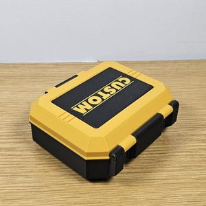 May include: A yellow and black plastic storage case with the word "CUSTOM" printed on the top.