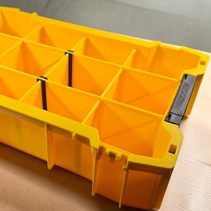 May include: A bright yellow rectangular storage organizer featuring multiple internal compartments separated by yellow dividers and thin black clips. The side of the unit displays the black text TOUGHSYSTEM embossed on a black plastic latch component.