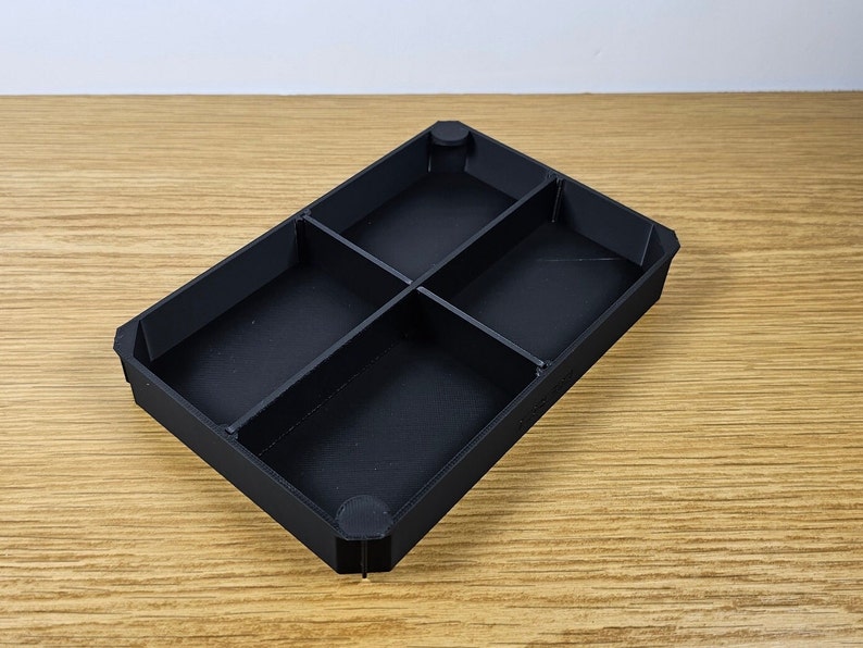 May include: Black plastic tray with four compartments. The tray is empty and has a rectangular shape.