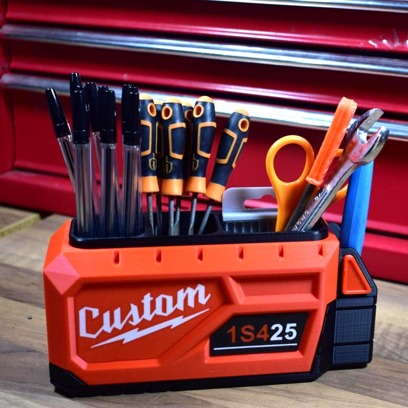 May include: An orange and black tool organizer with the word "Custom" and the numbers "1S425" printed on the front. The organizer holds various tools, including pens, screwdrivers, scissors, and a wrench.