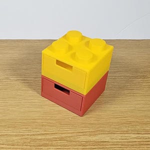 May include: Two stacked drawer organizers shaped like a yellow Lego brick. The top drawer is yellow and the bottom drawer is red.