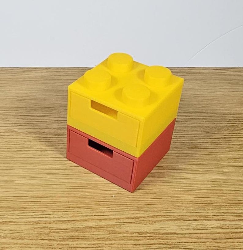 May include: Two stacked drawer organizers shaped like a yellow Lego brick. The top drawer is yellow and the bottom drawer is red.