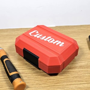 May include: A red plastic case with the word "Custom" printed in white on the top. The case is sitting on a wooden surface next to two screwdrivers.