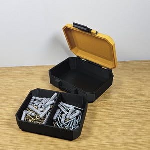 May include: A black plastic storage box with two compartments, one filled with silver and gold screws and the other with white plastic anchors. The box is open and the lid is yellow.
