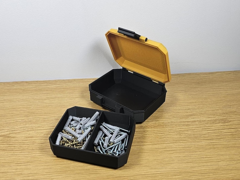 May include: A black plastic storage box with two compartments, one filled with silver and gold screws and the other with white plastic anchors. The box is open and the lid is yellow.
