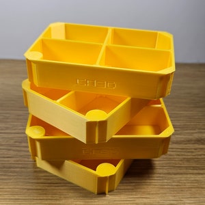 May include: Three stacked yellow plastic storage containers with multiple compartments. The containers are labelled "CREDO".