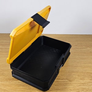 May include: A yellow plastic storage box with a black lid and a latch. The lid is open and the inside of the box is black.