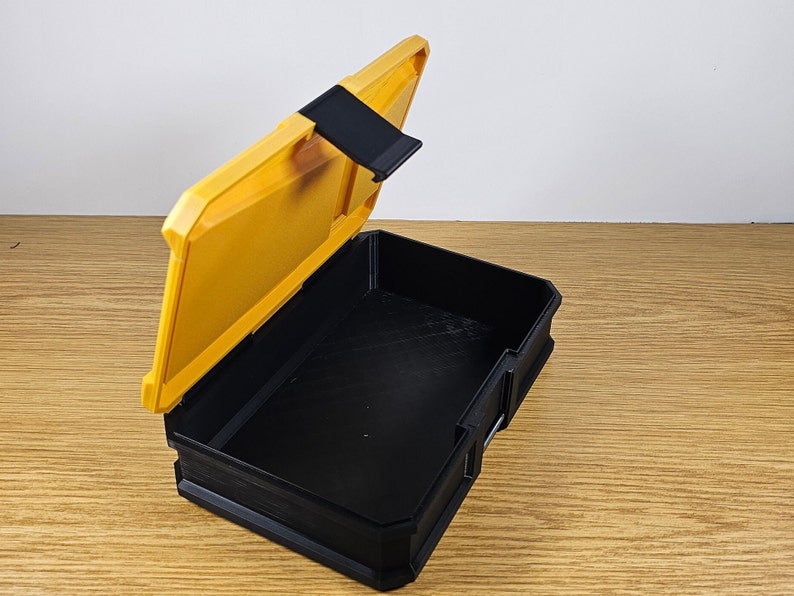 May include: A yellow plastic storage box with a black lid and a latch. The lid is open and the inside of the box is black.