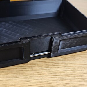 May include: A black plastic box with a silver metal latch. The box has a textured surface and is open.
