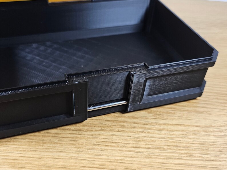 May include: A black plastic box with a silver metal latch. The box has a textured surface and is open.
