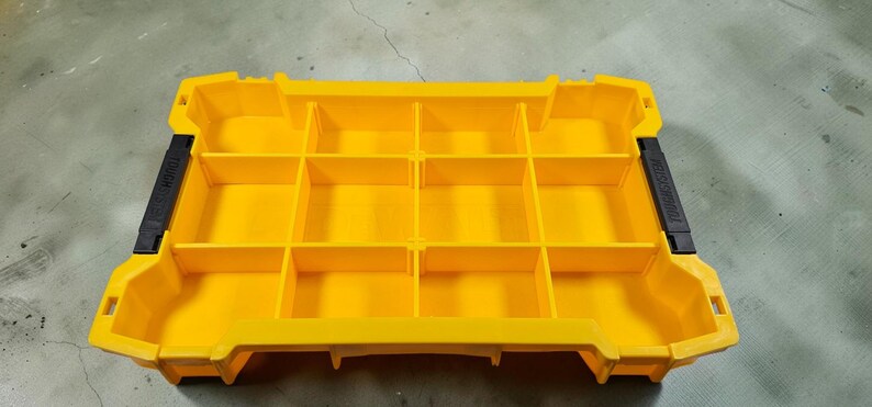 May include: A bright yellow storage container with multiple compartments. The container has a rectangular shape with a series of dividers creating individual storage spaces. Black handles are on each side. Ideal for organizing small items.
