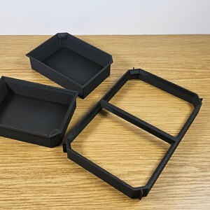 May include: Three black plastic trays, two are rectangular and one is square with a divider in the middle. The trays are empty and appear to be for organizing small items.