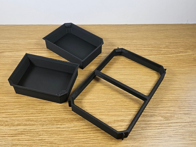 May include: Three black plastic trays, two are rectangular and one is square with a divider in the middle. The trays are empty and appear to be for organizing small items.
