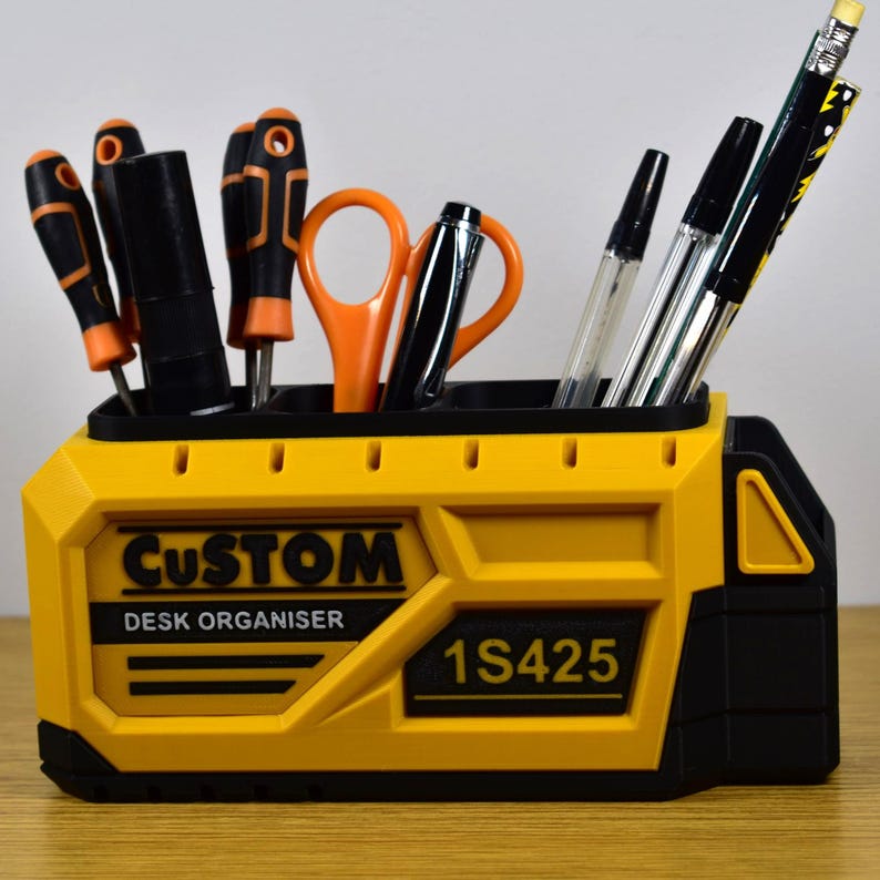 K&ouml;nnte beinhalten: Ein gelb-schwarzer Schreibtisch-Organizer mit den W&ouml;rtern "CUSTOM" und "DESK ORGANISER" auf der Vorderseite. Der Organizer enth&auml;lt verschiedene Werkzeuge, darunter Schraubendreher, Scheren, Stifte und Bleistifte. Die Modellnummer "1S425" ist ebenfalls sichtbar.