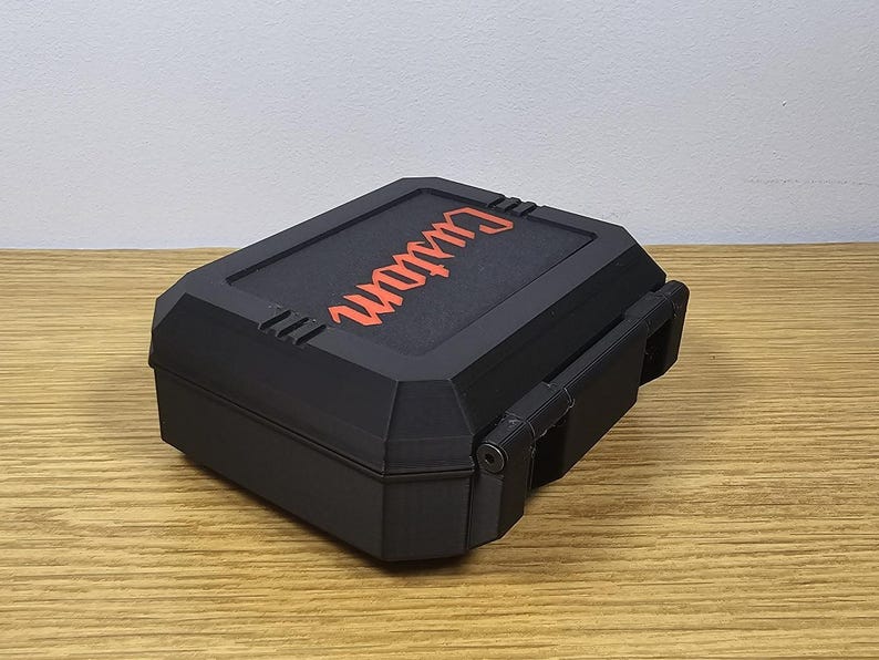 May include: Black rectangular box with the word "Custom" in orange lettering on the lid. The box has a hinged lid and a latch. The box is sitting on a wooden surface.
