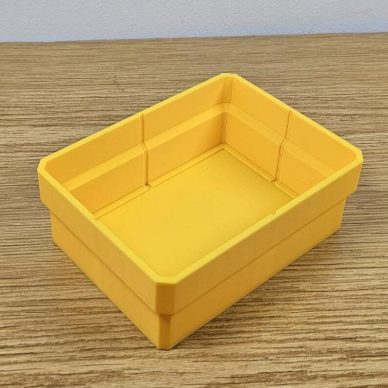 May include: A bright yellow rectangular storage bin with a slightly textured surface. The bin has a simple, modern design with straight sides and a flat bottom. The bin is made of a durable material and is suitable for organizing small items.