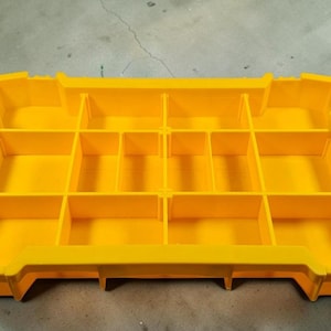 May include: A bright yellow parts organizer with multiple compartments. The organizer has a rectangular shape with black handles on each side. The compartments are divided by vertical and horizontal dividers, creating various storage spaces for small items.