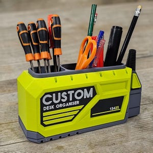 May include: A custom desk organizer in bright yellow and gray, holding various tools and stationery. The organizer features the text "CUSTOM DESK ORGANISER" and the number "1S425". It contains screwdrivers, scissors, pens, and a pencil.