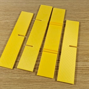 Op de afbeelding: Vijf gele plastic stukken met uitsparingen, mogelijk voor een knutselproject of een spel.