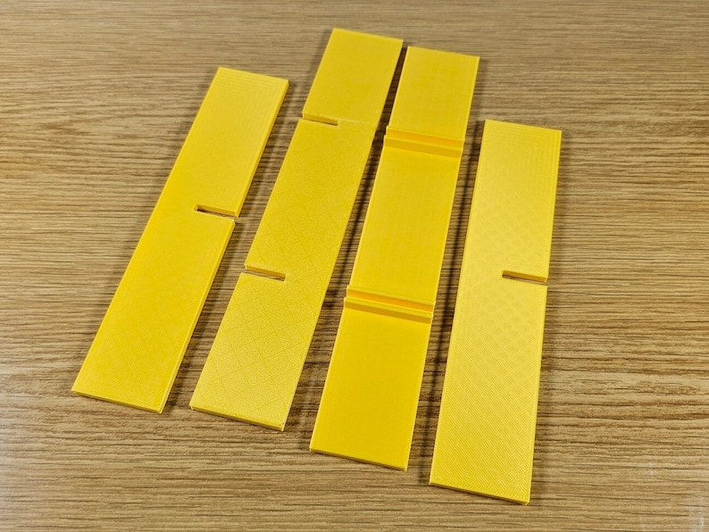 Op de afbeelding: Vijf gele plastic stukken met uitsparingen, mogelijk voor een knutselproject of een spel.