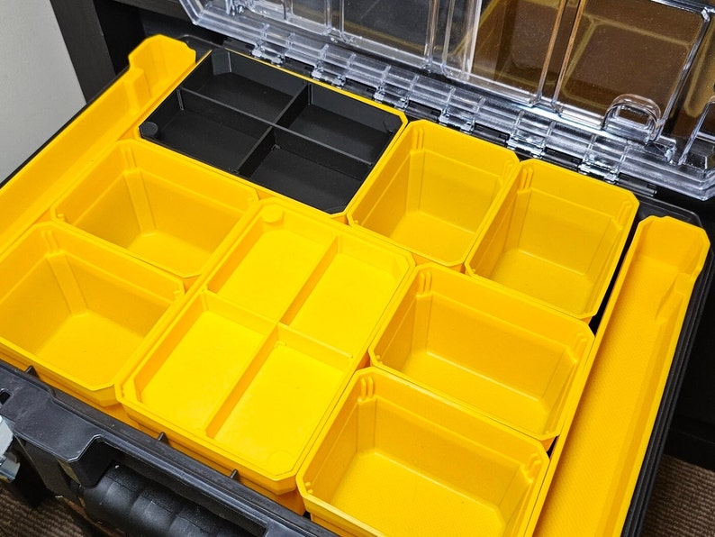 May include: An open black toolbox with multiple yellow plastic compartments. The compartments are various sizes and shapes, and some are divided into smaller sections.