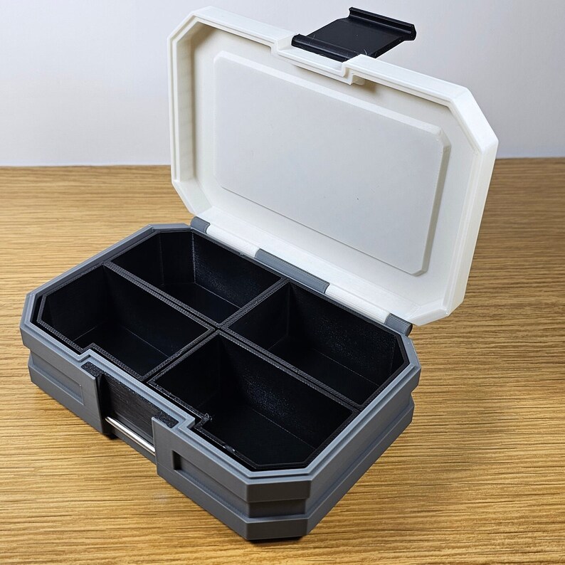 K&ouml;nnte beinhalten: Eine graue und wei&szlig;e Plastik-Aufbewahrungsbox mit einem Scharnierdeckel und mehreren F&auml;chern. Die Box ist ge&ouml;ffnet und die F&auml;cher sind leer.