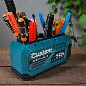 May include: A teal desk organizer with the word "Custom" and "DESK ORGANISER" printed on the front. The organizer holds various tools, pens, and scissors. The text "1S425" is also visible on the front.