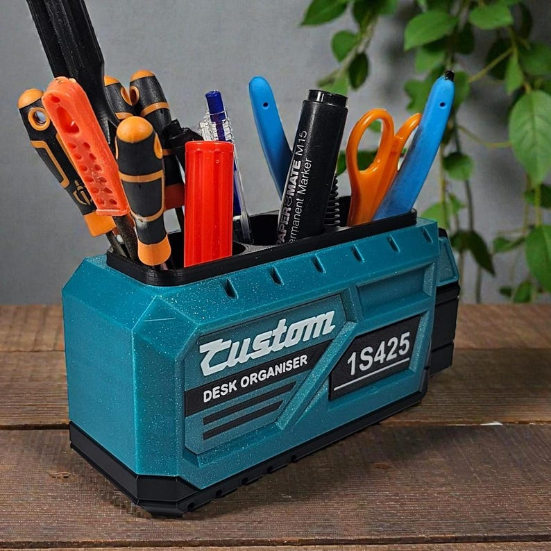 May include: A teal desk organizer with the word "Custom" and "DESK ORGANISER" printed on the front. The organizer holds various tools, pens, and scissors. The text "1S425" is also visible on the front.