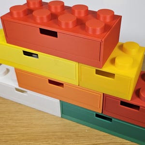 May include: Stack of six colorful drawer organizers shaped like Lego bricks. The drawers are red, yellow, orange, white, green, and red.