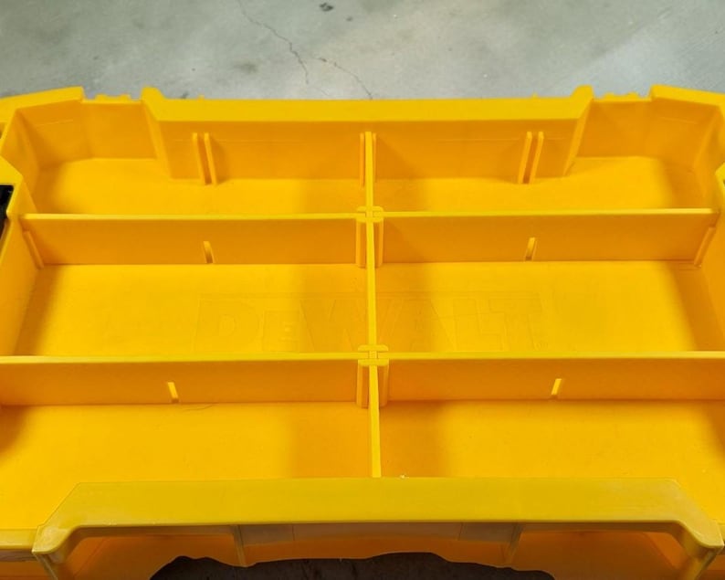 May include: A bright yellow plastic tool organiser with multiple compartments. The organiser has a rectangular shape with several dividers creating storage sections. It features a handle and a secure closure system for easy transport and organisation.