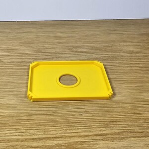 Pode incluir: Uma bandeja de pl&aacute;stico amarela com um recorte circular no centro. A bandeja tem uma borda ligeiramente elevada em torno do per&iacute;metro.