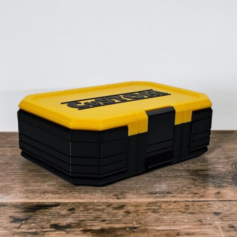 May include: A black and yellow storage box with the word "CUSTOM" on the lid. The box is rectangular with a yellow lid and black body. The box is sitting on a wooden surface.