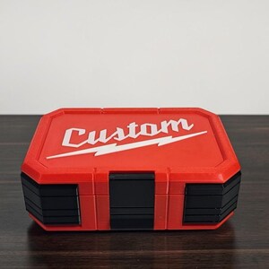 May include: A red and black toolbox with the word "Custom" in white script. The toolbox features a lightning bolt design. The rectangular box is made of plastic with black accents and is designed for tools.