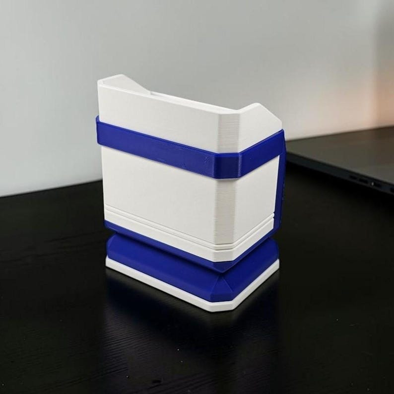 May include: A 3D-printed, geometric container with a white body and blue accents. The container has a rectangular shape with a blue band around the middle and a blue base. The top has a unique, angled design.