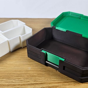 May include: Two 3D printed storage boxes. One box is white with four compartments and the other is black with a green lid.