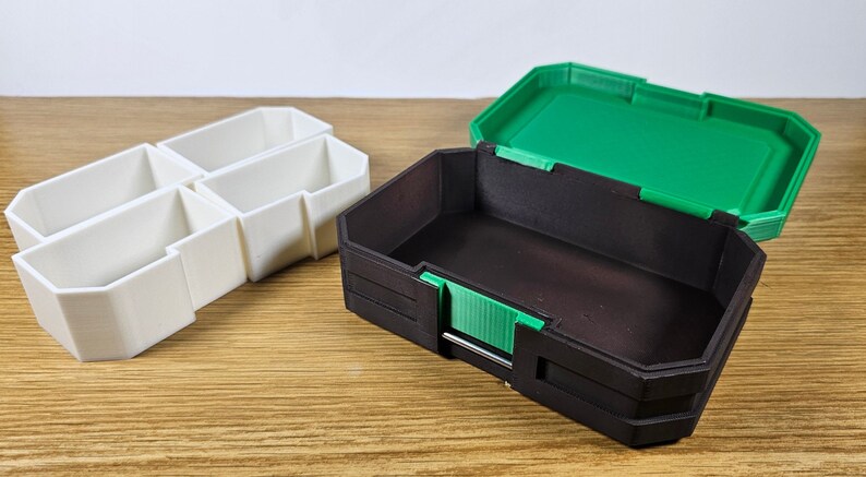 May include: Two 3D printed storage boxes. One box is white with four compartments and the other is black with a green lid.
