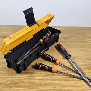 May include: A yellow and black tool box with a black handle, open to reveal a set of metal files. Four files are laying outside the box on a wooden surface.