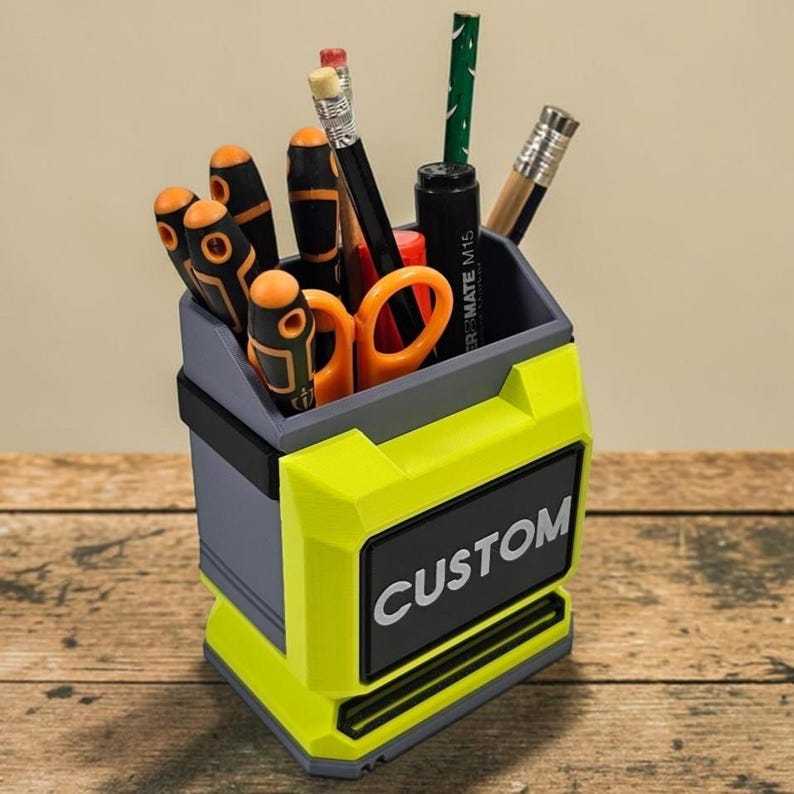 May include: A custom desk tidy in grey and neon yellow, containing tools and stationery. The organiser has the word "CUSTOM" in white on a black label. Contents include screwdrivers, scissors, pencils, and a pen.
