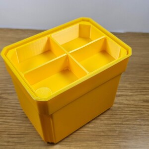 May include: A yellow plastic storage box with four compartments. The box is empty and has a smooth surface.