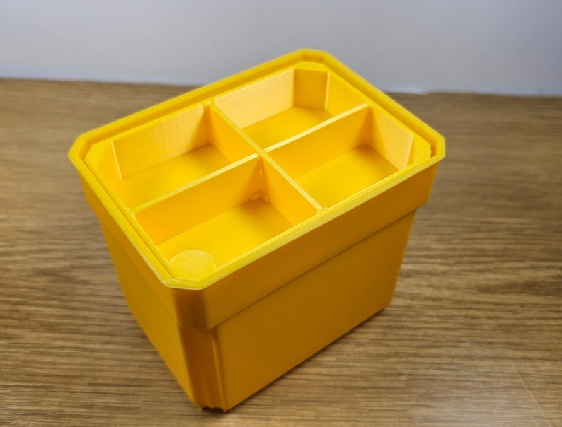 May include: A yellow plastic storage box with four compartments. The box is empty and has a smooth surface.
