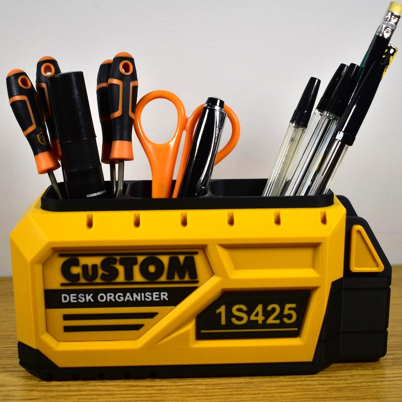 K&ouml;nnte beinhalten: Ein gelb-schwarzer Schreibtisch-Organizer mit den W&ouml;rtern "CUSTOM" und "DESK ORGANISER" auf der Vorderseite. Er enth&auml;lt Schraubendreher, Scheren, Stifte und Bleistifte. Die Modellnummer "1S425" ist ebenfalls aufgedruckt.